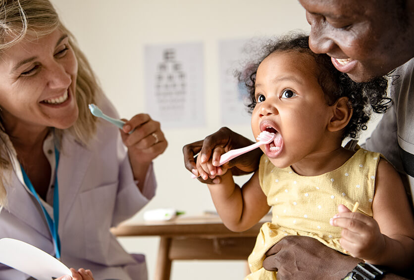 dentist showing a little girl how to brush her teeth