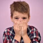 Young boy covers his mouth because he doesn't brush his teeth and is experiencing oral health problems