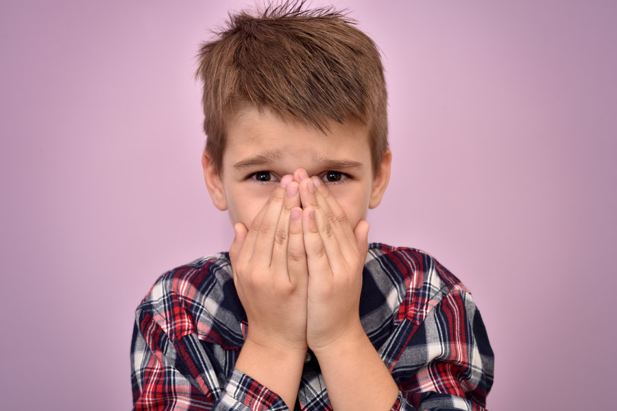 Young boy covers his mouth because he doesn't brush his teeth and is experiencing oral health problems